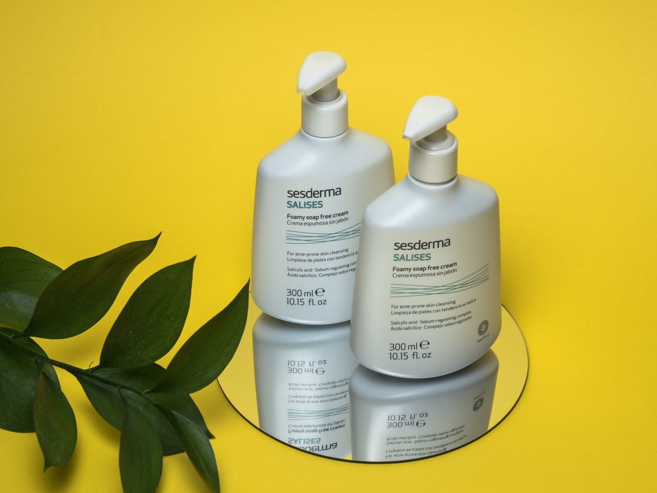 Services Minimalist skincare product bottles on a mirror with leaves on a yellow backdrop.